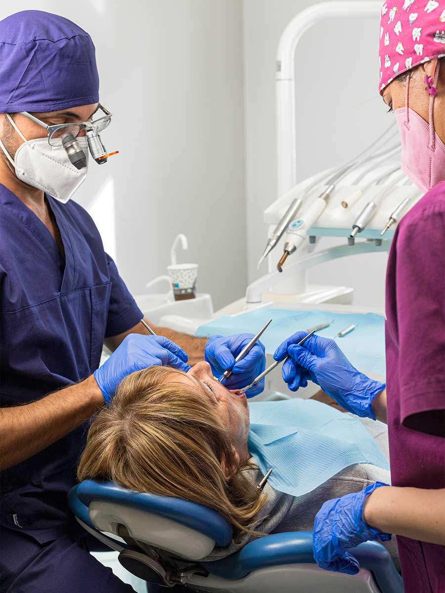 Dentista e assistente in camice blu e rosa, mascherine e guanti, curano una paziente sdraiata su una poltrona odontoiatrica. Dentista e assistente in camice blu e rosa, mascherine e guanti, curano una paziente sdraiata su una poltrona odontoiatrica.
