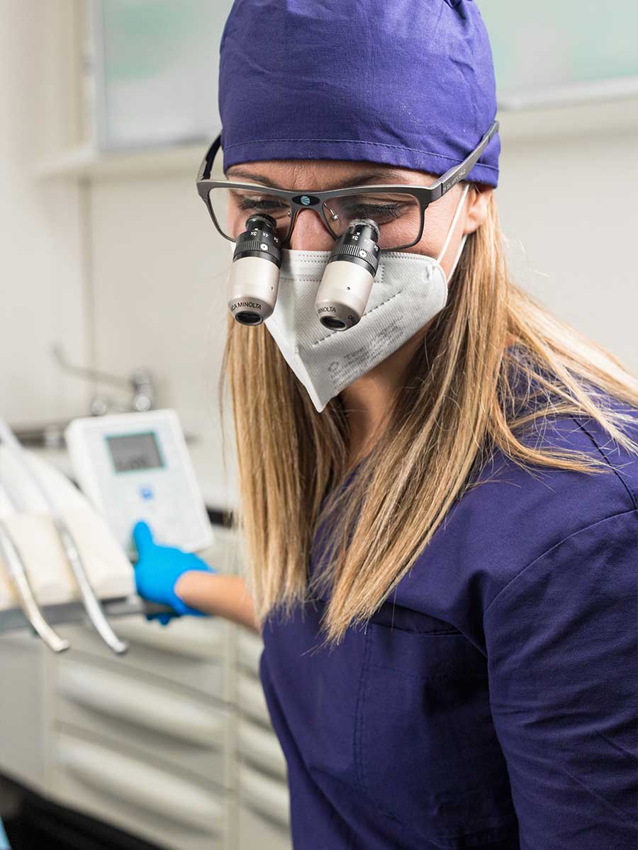 Professionista medico con camice blu, cuffia, mascherina FFP2 e guanti. Indossa occhiali con lenti ingrandenti Minolta, aziona un dispositivo. Professionista medico con camice blu, cuffia, mascherina FFP2 e guanti. Indossa occhiali con lenti ingrandenti Minolta, aziona un dispositivo.