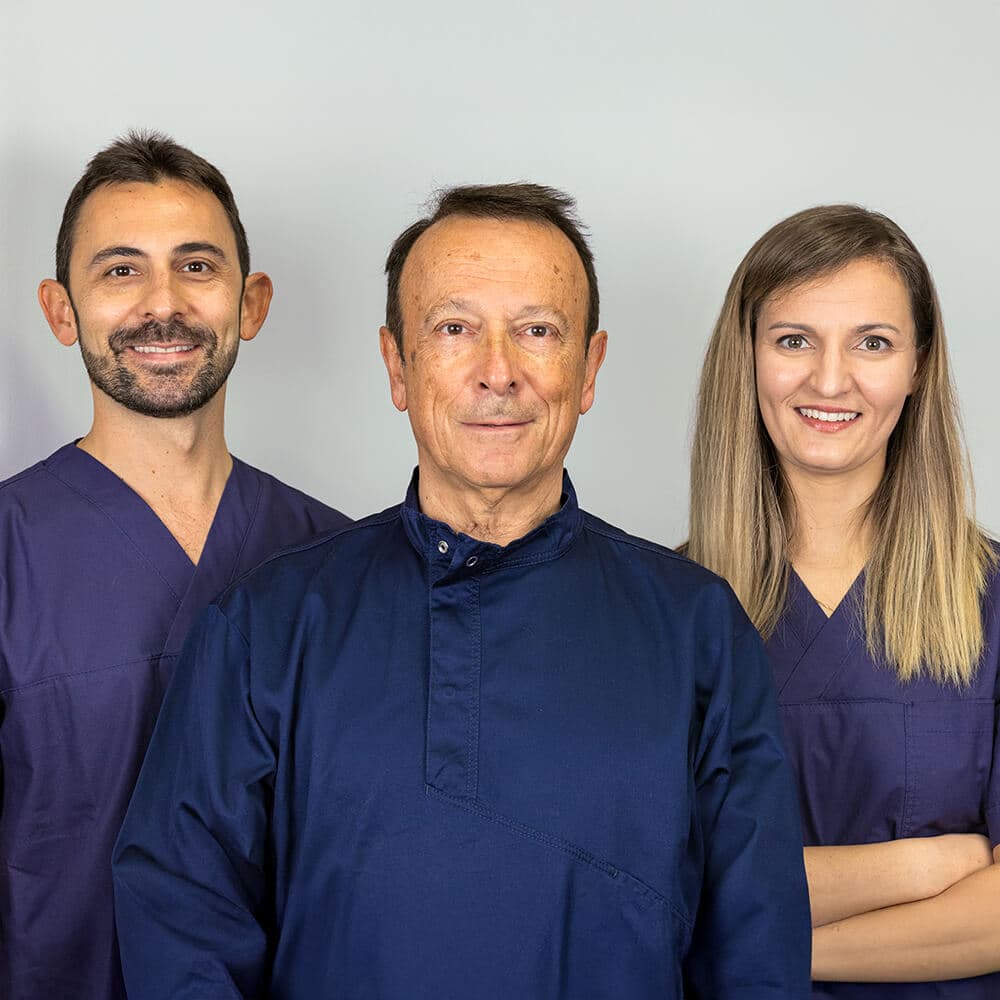 Tre professionisti sanitari in divisa blu, due uomini e una donna, sorridono davanti a uno sfondo grigio chiaro. Tre professionisti sanitari in divisa blu, due uomini e una donna, sorridono davanti a uno sfondo grigio chiaro.